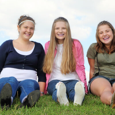 Tre galde jenter sitter på gresset.