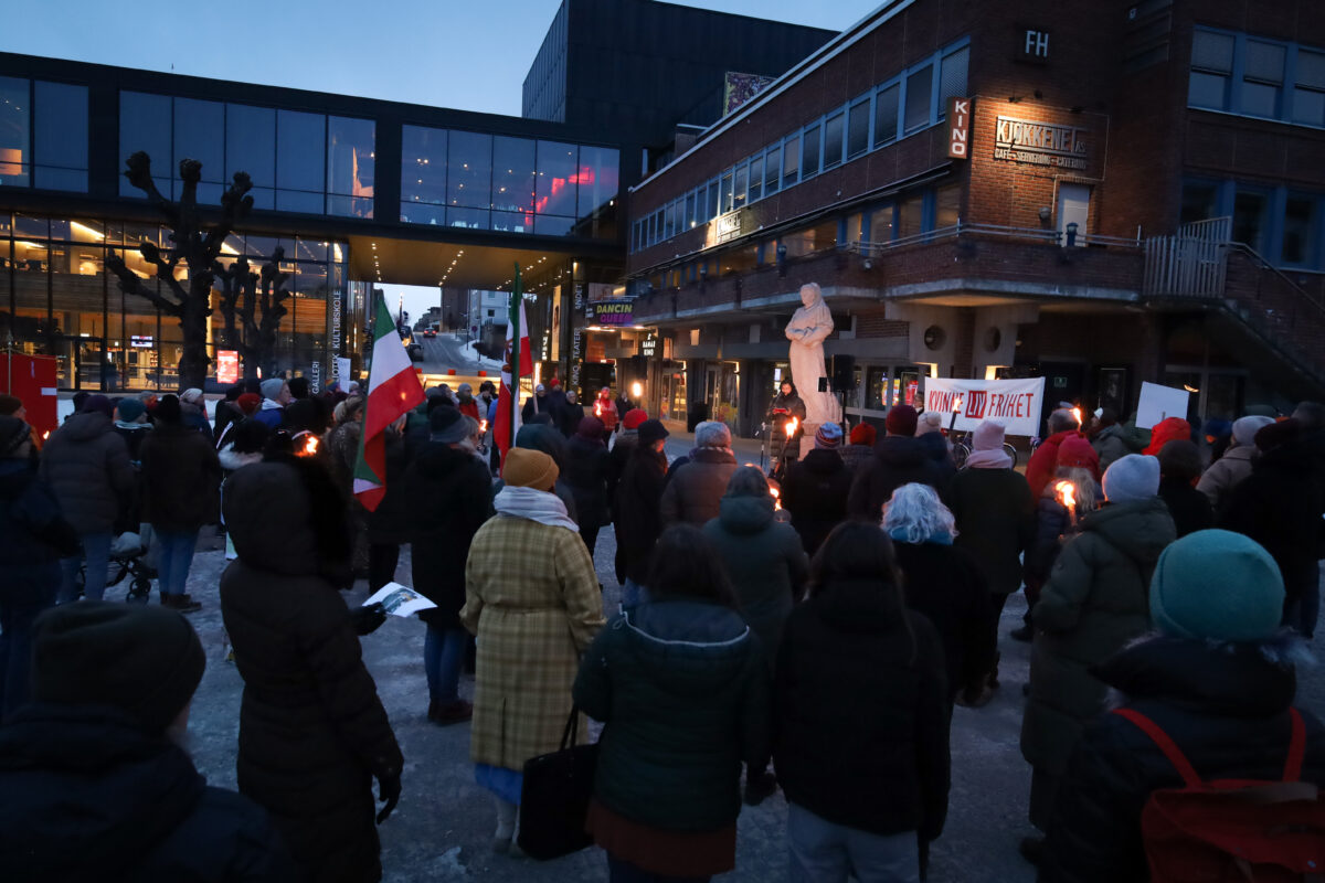
			Ansamling mennesker utenfor Hamar kulturhus med fakler, som hører på en 8. mars-taler.			