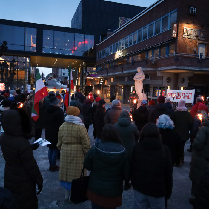 Ansamling mennesker utenfor Hamar kulturhus med fakler, som hører på en 8. mars-taler.
